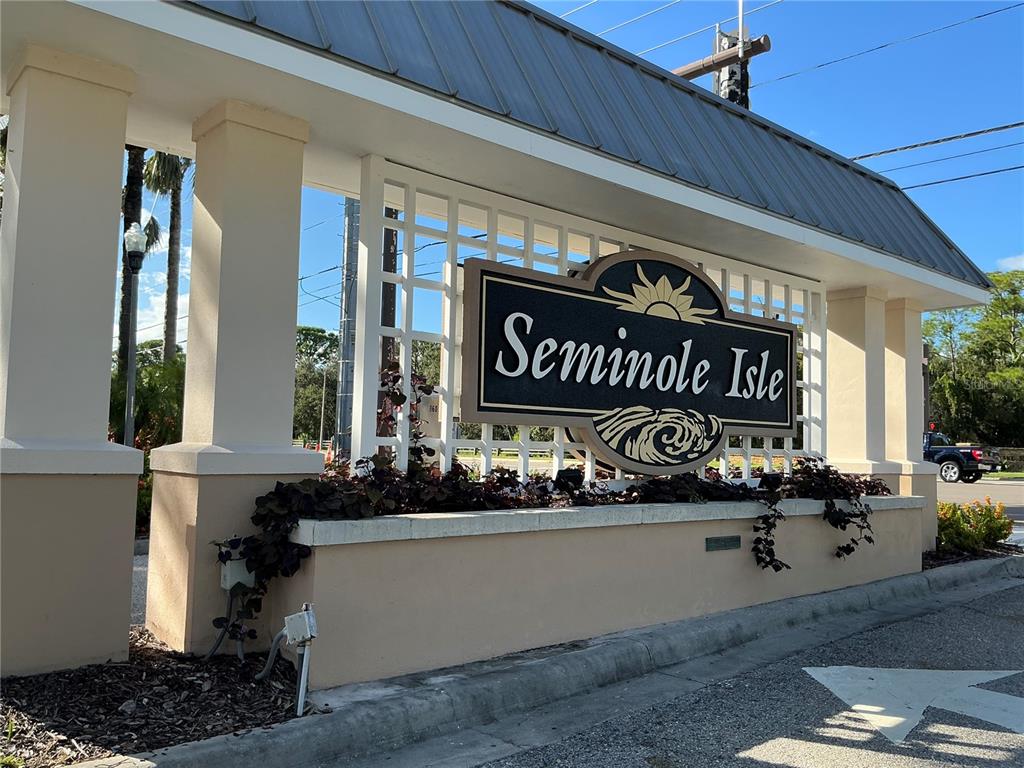 A beige stucco entrance sign for Seminole Isle features a dark plaque with gold lettering — 7059 ISLAMORADA CIRCLE, SEMINOLE, FL