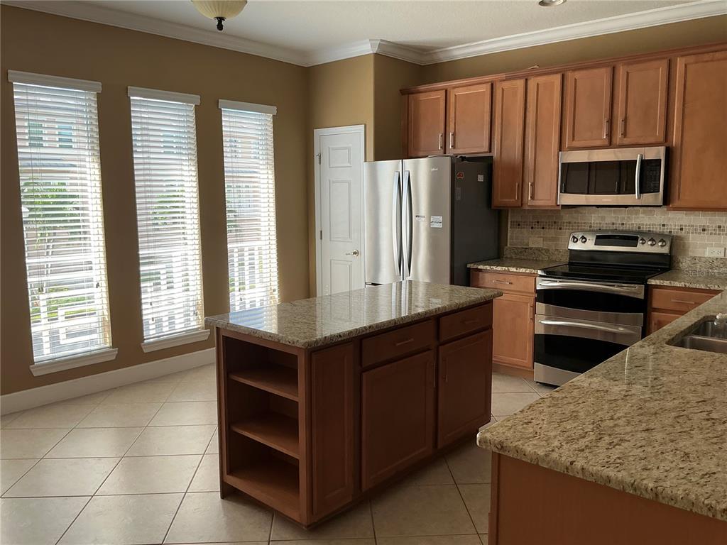 A kitchen with wood cabinets, granite countertops, a center island, and three large windows — 7059 ISLAMORADA CIRCLE, SEMINOLE, FL