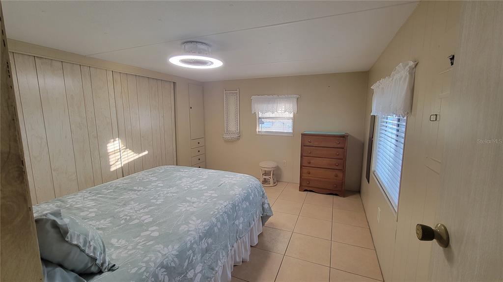A bedroom features tile flooring, a bed with a floral quilt, and wood-paneled walls — 60 5TH STREET, PUNTA GORDA, FL