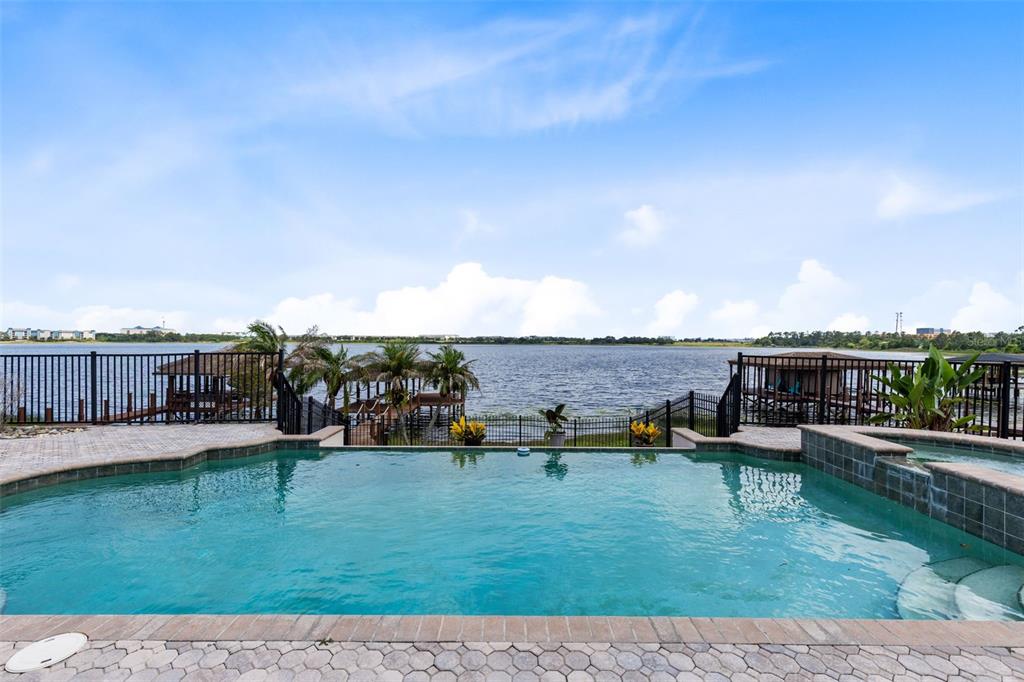An infinity-edge swimming pool overlooks a lake with docks and a black metal fence — 10273 COVE LAKE DRIVE, ORLANDO, FL