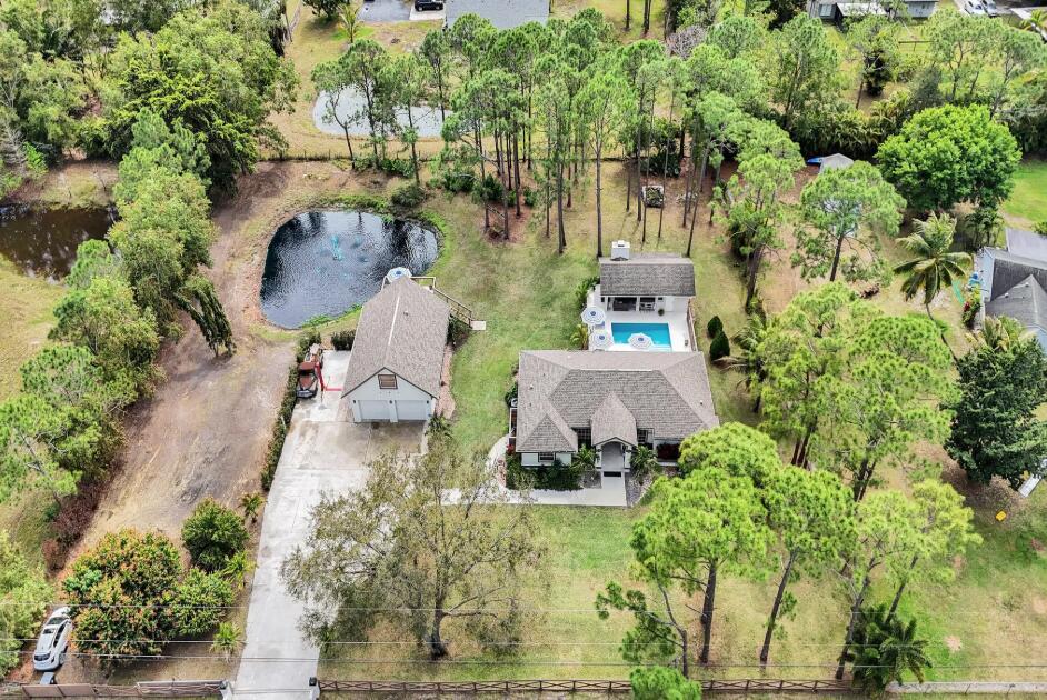 An aerial view of a house with a pool, detached garage, and pond on wooded land — 14648 88th Place N, FL 33470, FL