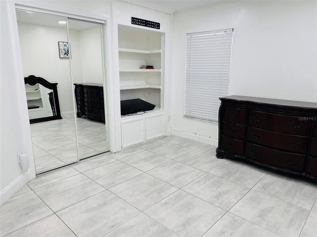 A bedroom features white walls, light tile flooring, a mirrored closet, and built-in shelving — 925 PEBBLE CREEK CIRCLE, ORLANDO, FL