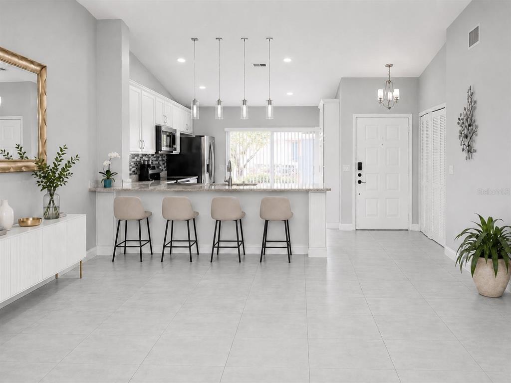A bright kitchen with white cabinets, a breakfast bar with four stools, and tile flooring — 925 PEBBLE CREEK CIRCLE, ORLANDO, FL