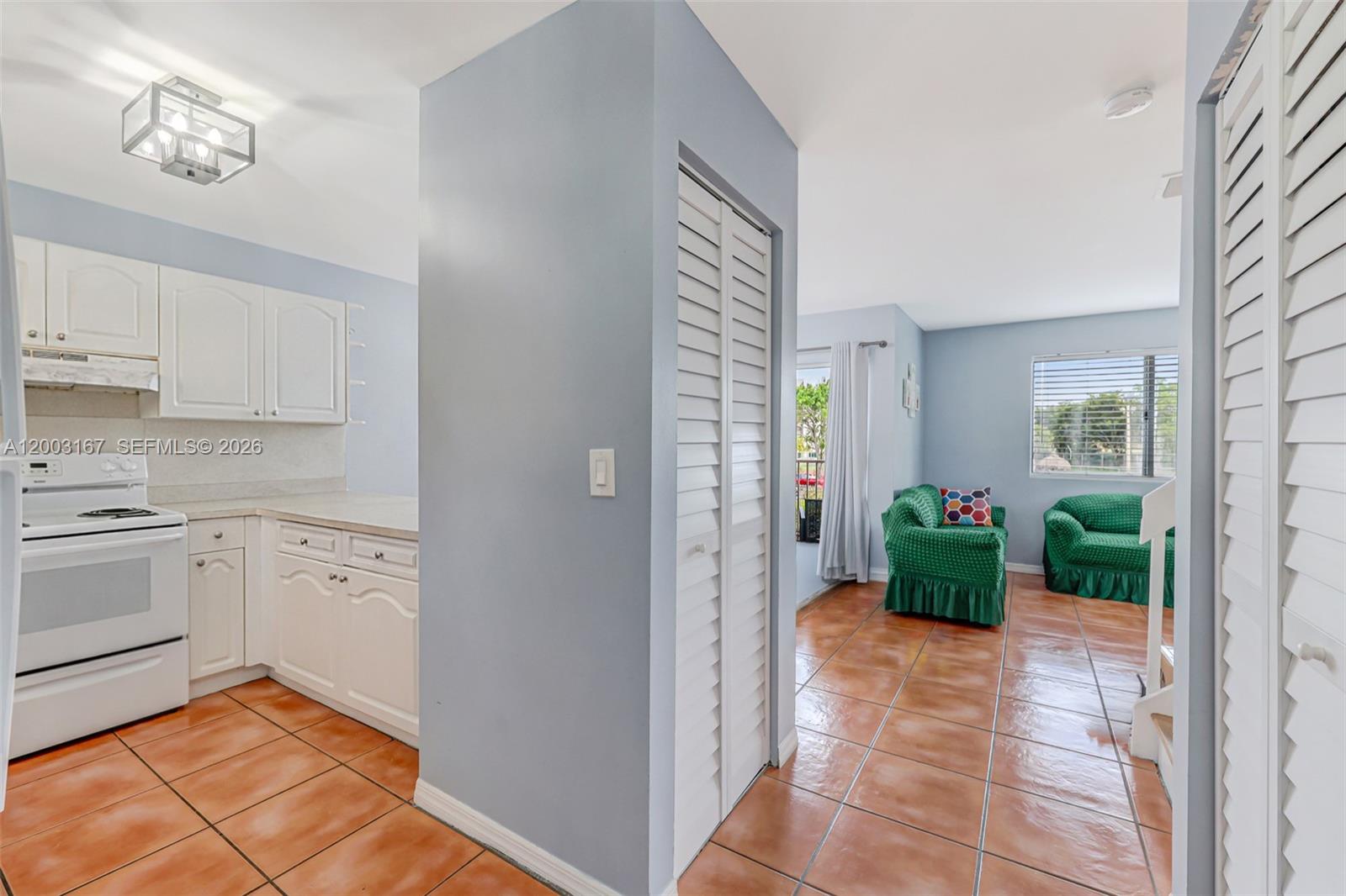 A kitchen with white cabinets and tile floors opens into a living area with furniture — 6255 Kendale Lakes Cir # 218, Miami FL 33183, MIAMI, FL