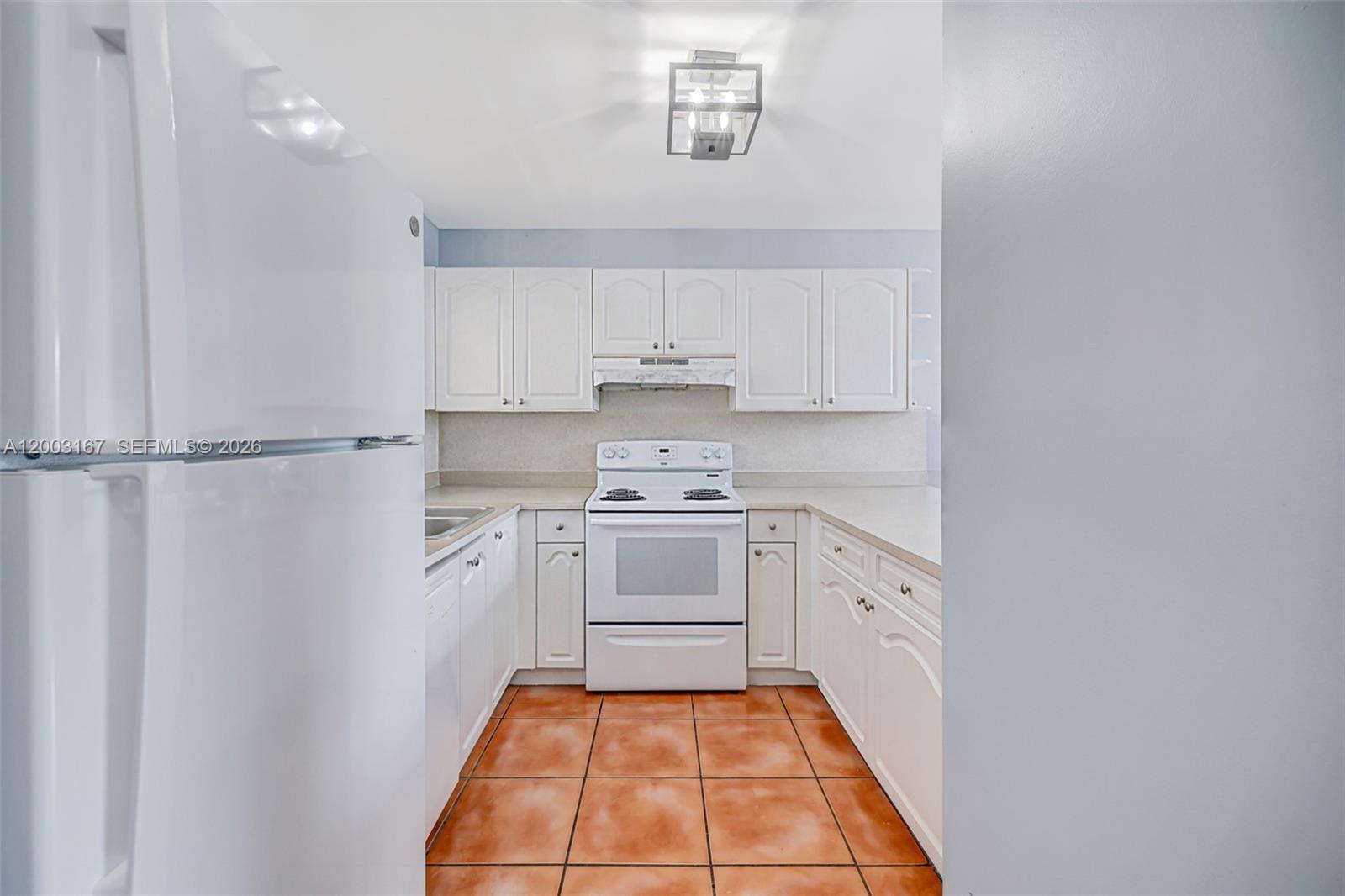 A galley kitchen features white cabinets, white appliances, and orange tile flooring — 6255 Kendale Lakes Cir # 218, Miami FL 33183, MIAMI, FL