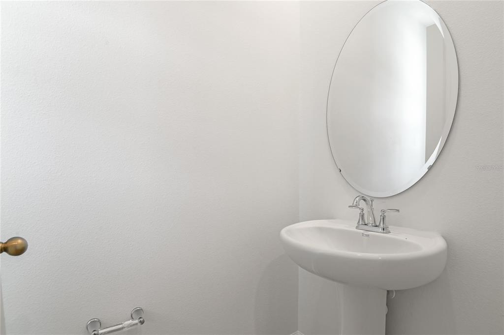 A minimalist powder room features a white pedestal sink, an oval mirror, and light walls — 742 LAKE DELL AVENUE, DUNDEE, FL