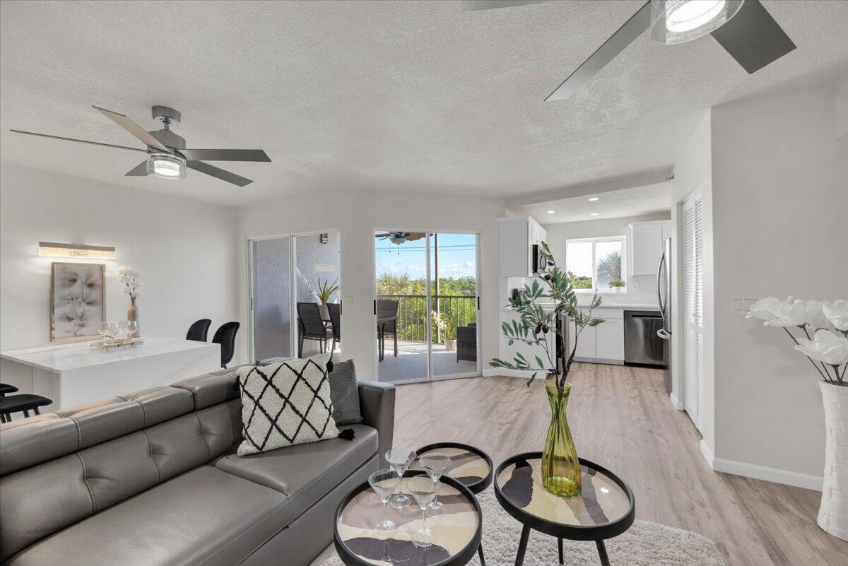 A living room with a grey sofa, wood-look flooring, and a sliding door to a balcony — 275 Palm Avenue # B304, Jupiter FL 33477, JUPITER, FL