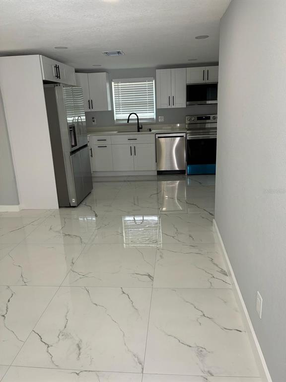 A kitchen features white cabinets, stainless steel appliances, and large white marble-patterned floor tiles — 8290 OSPREY ROAD, ENGLEWOOD, FL