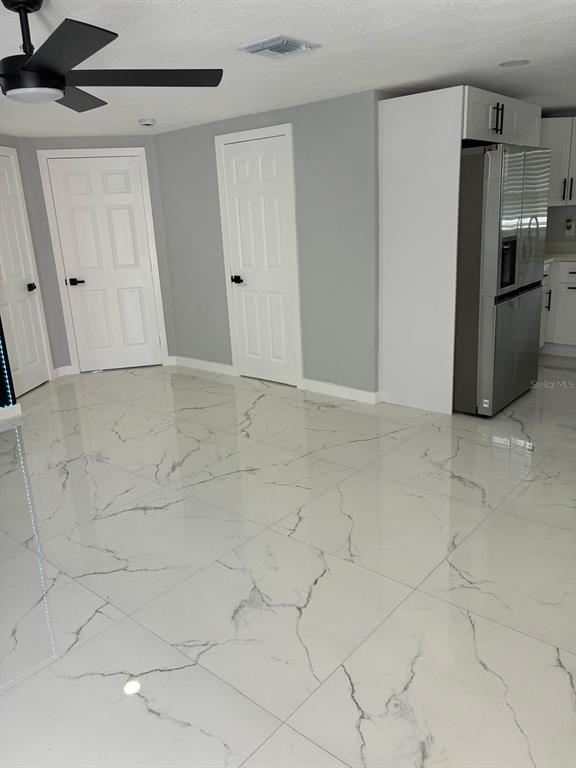 A room with white marble-patterned tile flooring, two white doors, and a stainless steel refrigerator — 8290 OSPREY ROAD, ENGLEWOOD, FL