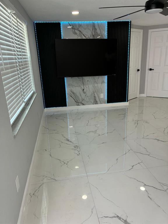 A room with white marble-patterned tile floors and a wall-mounted television on a marble accent wall — 8290 OSPREY ROAD, ENGLEWOOD, FL