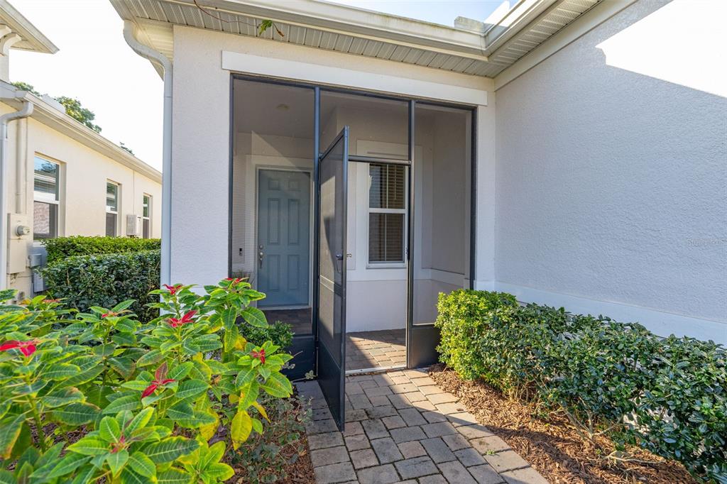 A paved walkway leads to a screened-in entryway with a blue front door — 1855 FLORA PASS PLACE, KISSIMMEE, FL