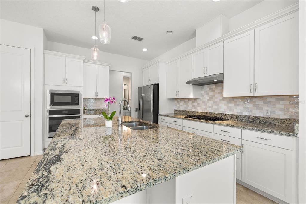 A modern kitchen features white cabinetry, granite countertops, a large island, and stainless steel appliances — 1855 FLORA PASS PLACE, KISSIMMEE, FL