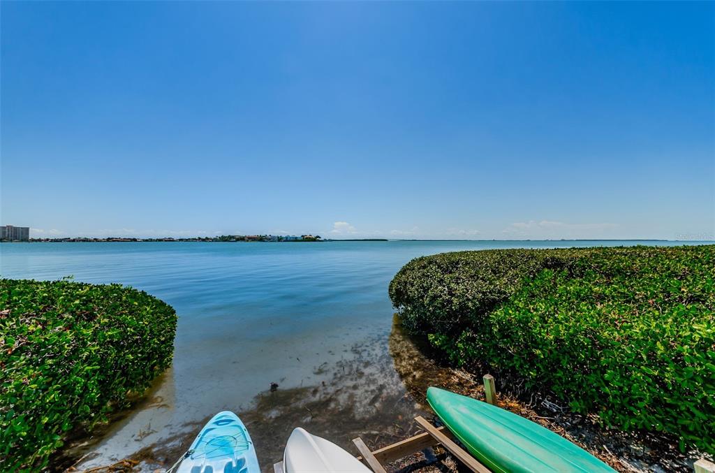A view of a calm bay with kayaks resting on the shore near green bushes — 6268 PALMA DEL MAR BOULEVARD S UNIT 102, ST PETERSBURG, FL