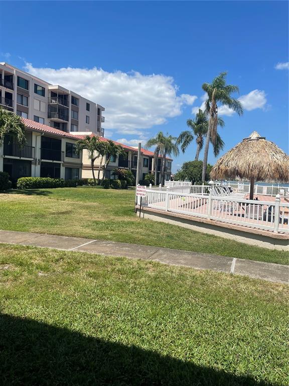 A multi-story apartment building stands next to a grassy lawn and a fenced pool area — 6268 PALMA DEL MAR BOULEVARD S UNIT 102, ST PETERSBURG, FL