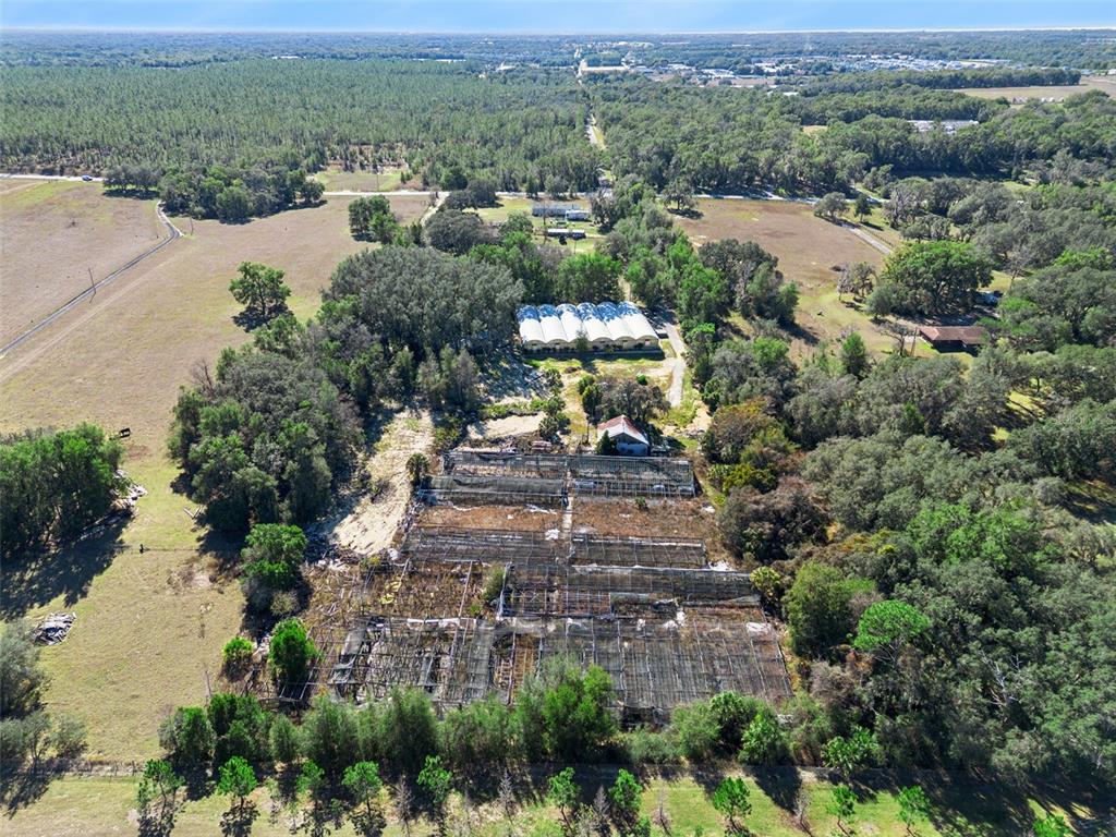 An aerial view shows a rural property with greenhouses, a warehouse, and surrounding wooded land — 1909 HAAS ROAD, APOPKA, FL