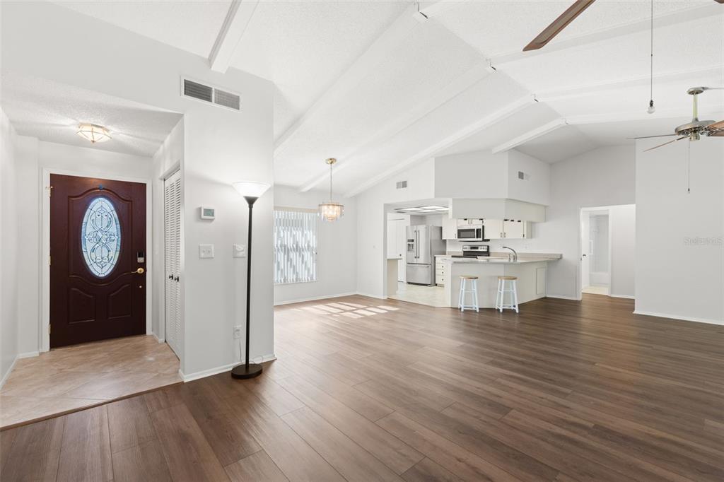 An open-concept living area features wood-look flooring, vaulted ceilings, and a kitchen with bar seating — 3420 HYDE PARK DRIVE, CLEARWATER, FL