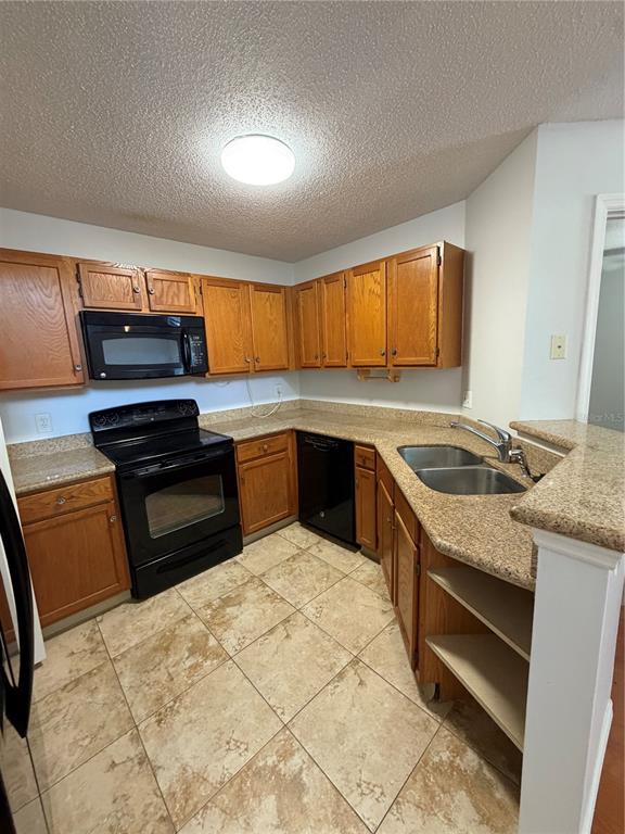 A kitchen features oak cabinets, black appliances, granite countertops, and light-colored tile flooring — 949 BIRD BAY COURT UNIT 201, LAKE MARY, FL