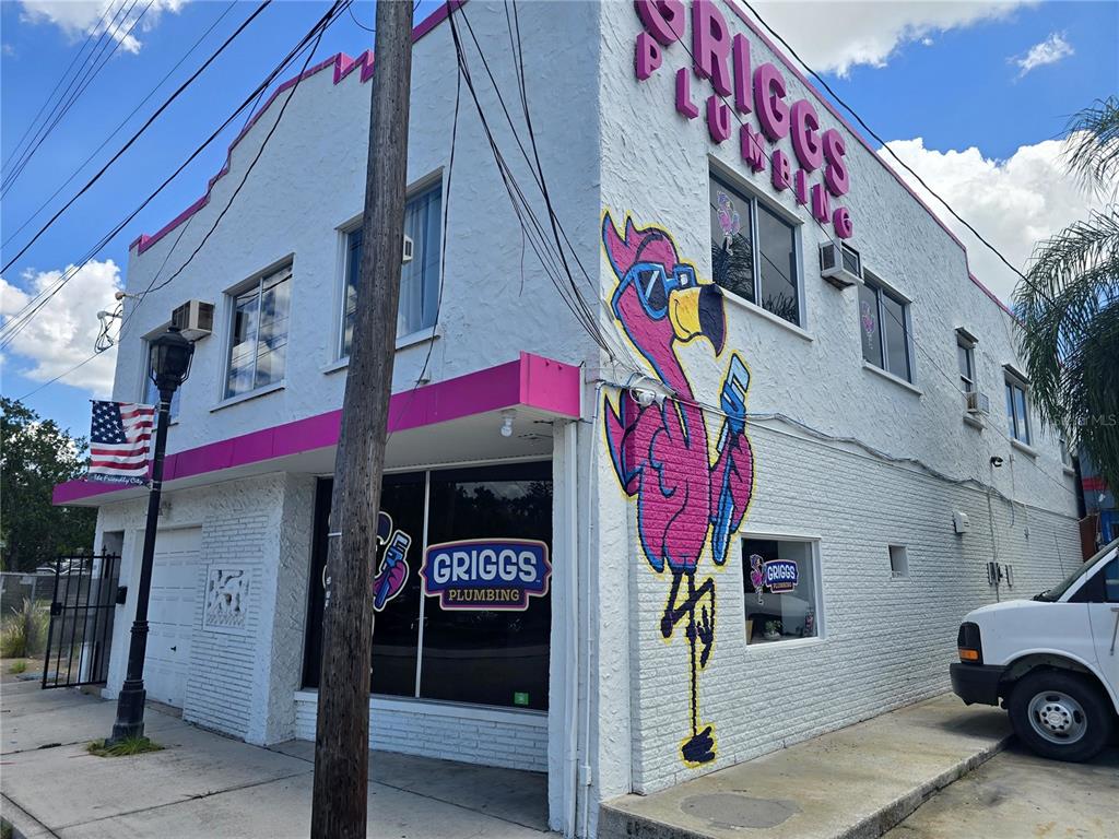 A two-story white building features a large flamingo mural and signage for Griggs Plumbing — 1315 12TH AVENUE W, BRADENTON, FL