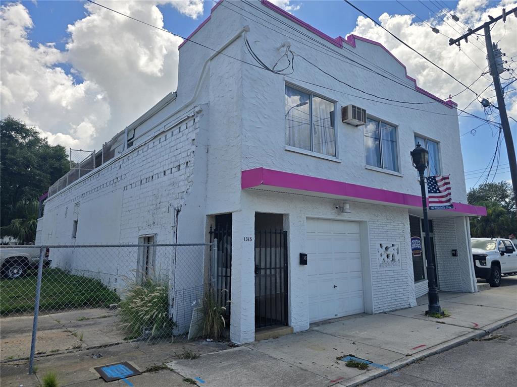 A two-story white building with a pink awning and a garage door sits on a street — 1315 12TH AVENUE W, BRADENTON, FL