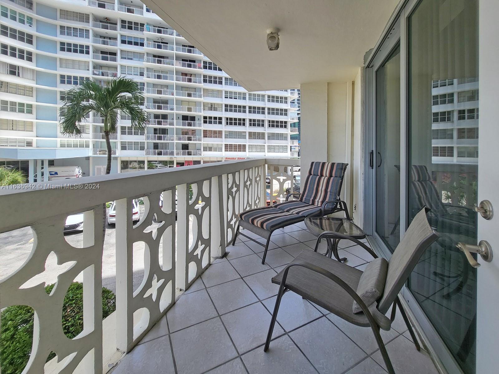 A balcony with tiled flooring, outdoor furniture, and a decorative railing overlooking a parking area — 1825 S Ocean Dr # 206, Hallandale Beach FL 33009, HALLANDALE BEACH, FL