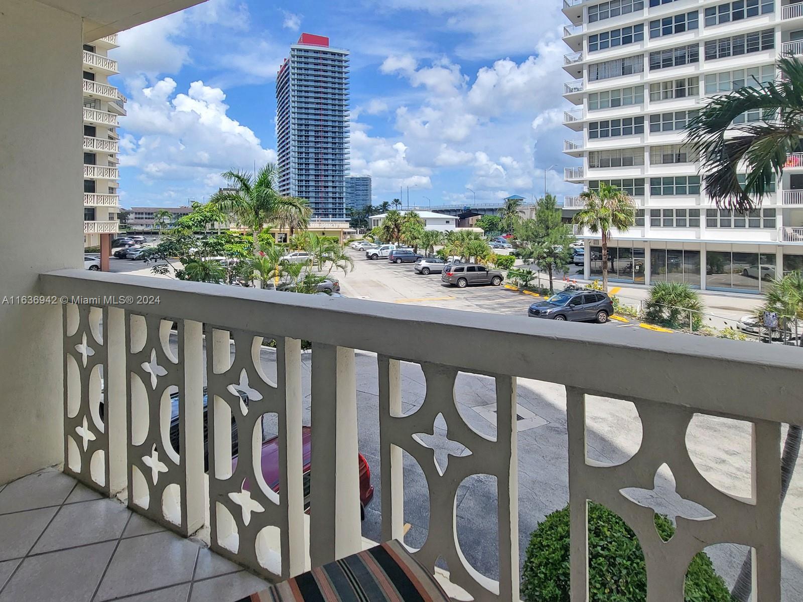 A balcony with a decorative railing overlooks a parking lot and surrounding high-rise buildings — 1825 S Ocean Dr # 206, Hallandale Beach FL 33009, HALLANDALE BEACH, FL