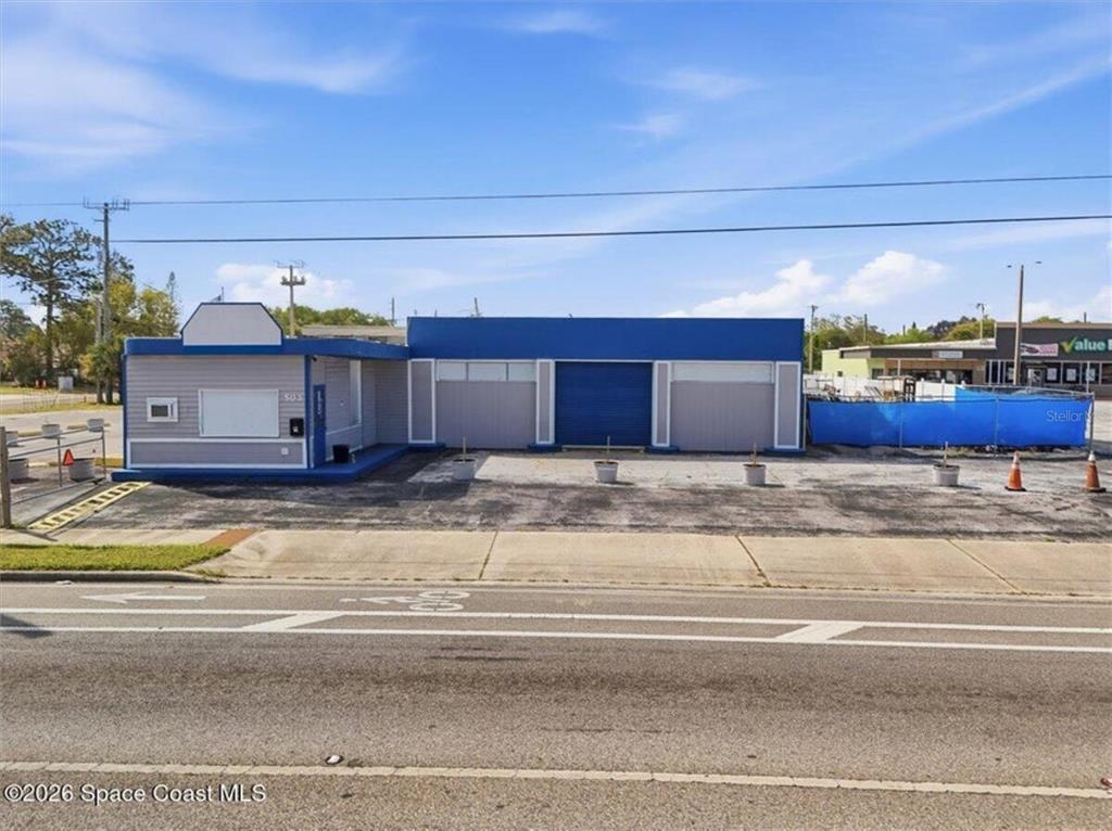 A single-story commercial building with a blue facade and three garage bays faces a road — 503 CHENEY HIGHWAY, TITUSVILLE, FL