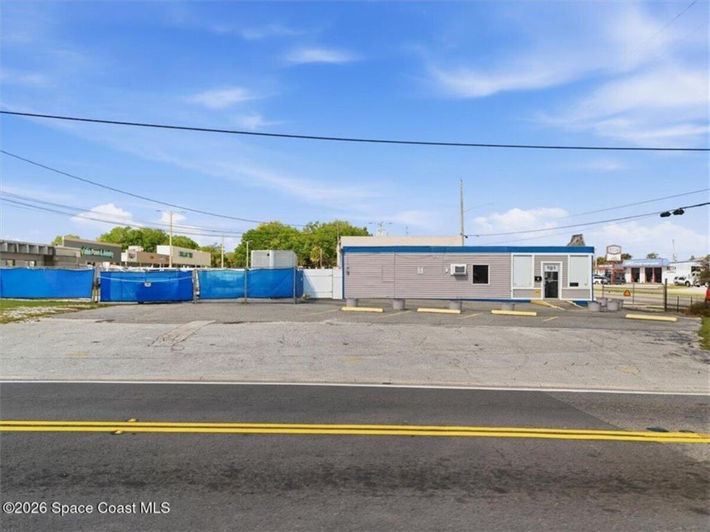 A single-story commercial building sits behind a paved parking lot and blue construction fencing — 503 CHENEY HIGHWAY, TITUSVILLE, FL