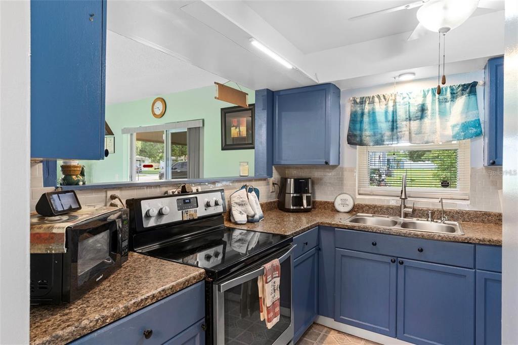 A kitchen features blue cabinets, granite-look countertops, a stainless steel stove, and a double sink — 1566 PROVIDENCE BOULEVARD, DELTONA, FL