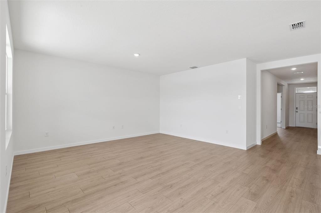 An empty room with light wood-look flooring and white walls leads to an entryway — 6726 SCRUB HICKORY AVENUE, APOPKA, FL