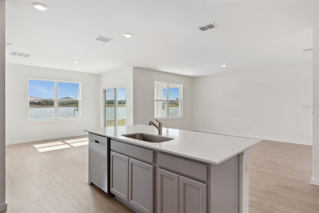 A kitchen island with a stainless steel sink and dishwasher faces a bright living area — 6726 SCRUB HICKORY AVENUE, APOPKA, FL