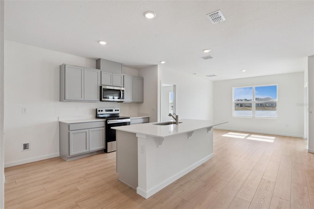 A modern kitchen features gray cabinets, white countertops, a central island, and light wood flooring — 6726 SCRUB HICKORY AVENUE, APOPKA, FL