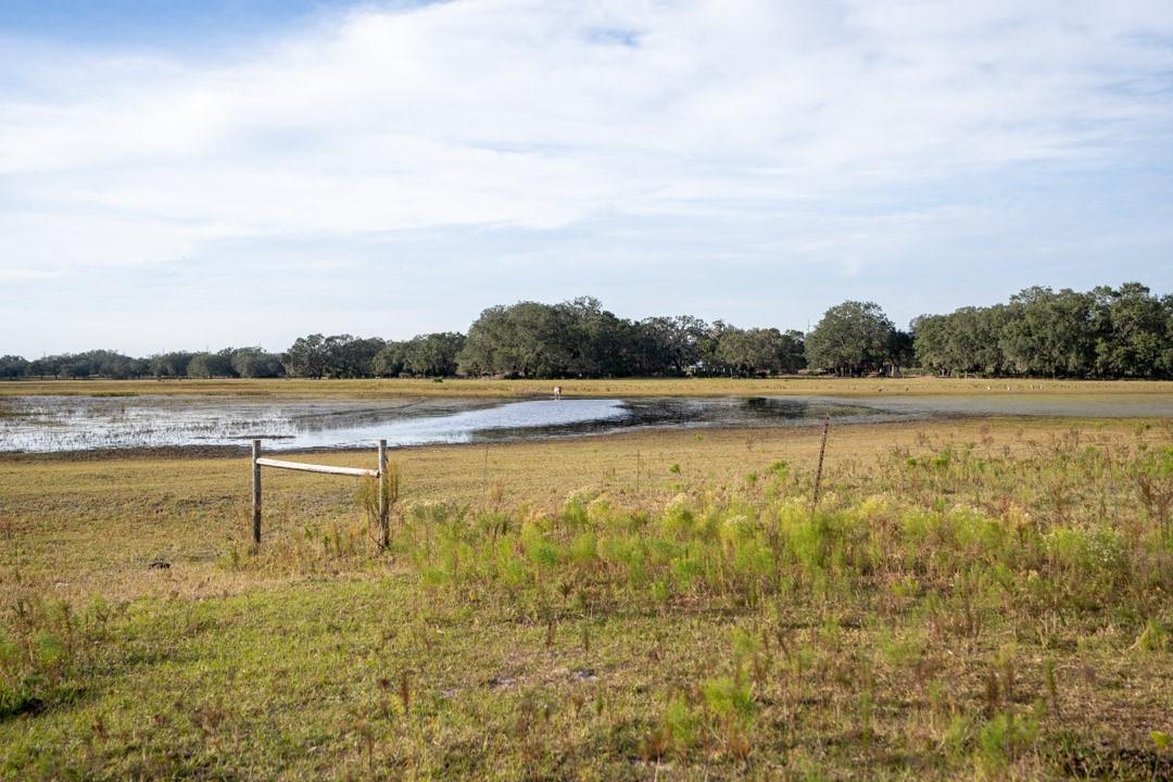 A grassy field with a small pond and a wooden fence under a cloudy sky — 0 Lake Hatcheneha, FL 33844, FL