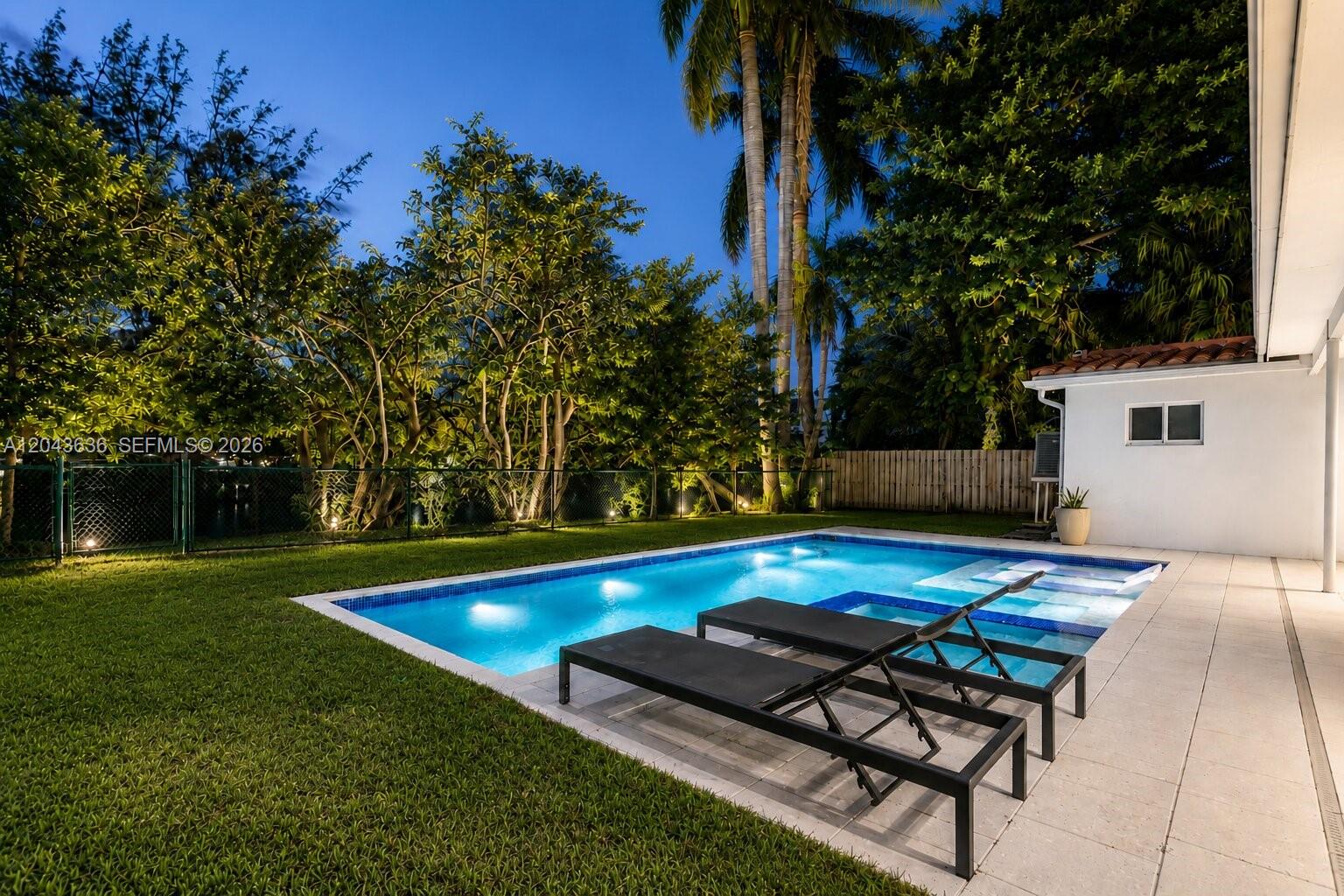 A swimming pool with lounge chairs sits in a backyard at dusk — 200 NW 86th St, El Portal FL 33138, EL PORTAL, FL