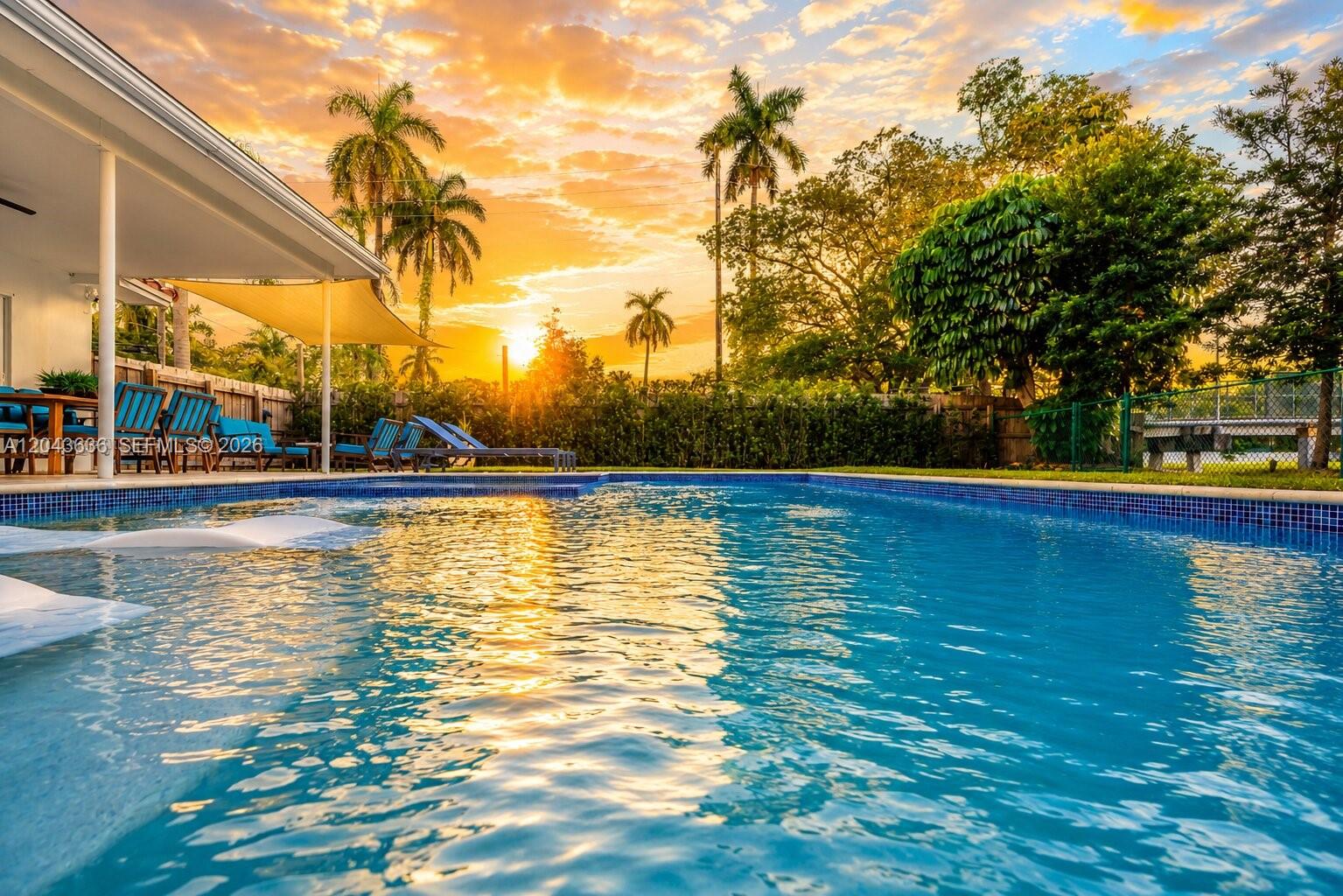 A swimming pool with lounge chairs on a patio under a sunset sky — 200 NW 86th St, El Portal FL 33138, EL PORTAL, FL