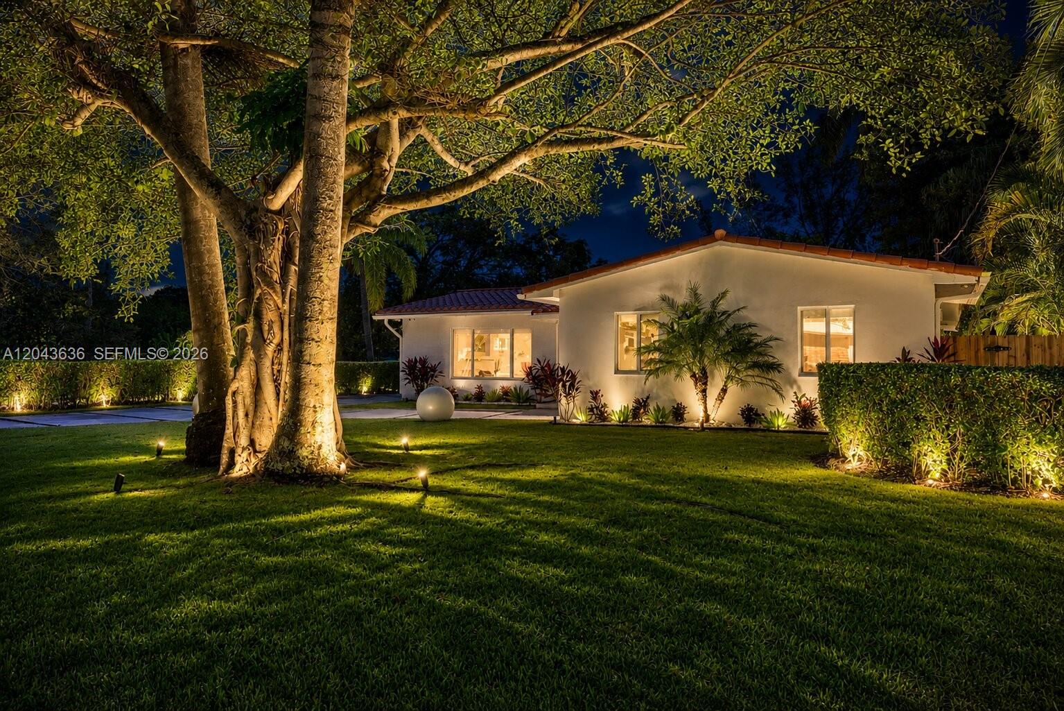 A white house with a tile roof is illuminated at night behind a large tree — 200 NW 86th St, El Portal FL 33138, EL PORTAL, FL
