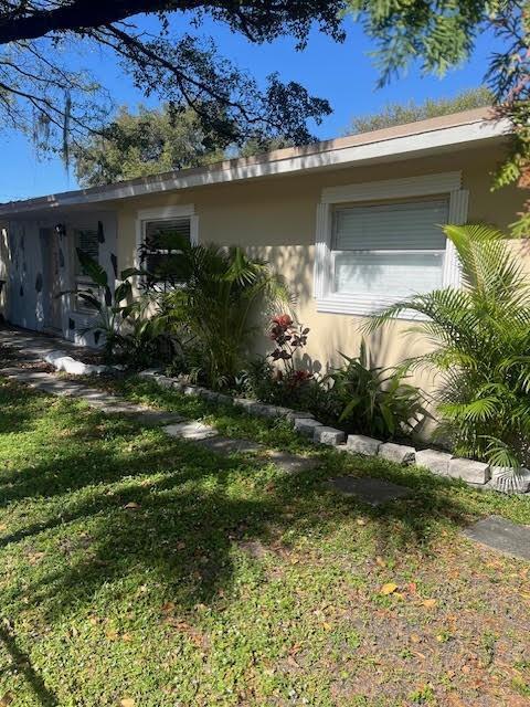 A single-story house exterior features tan siding, a white-trimmed window, and various green plants — 734 SW 8th Street, Dania Beach FL 33004, DANIA BEACH, FL