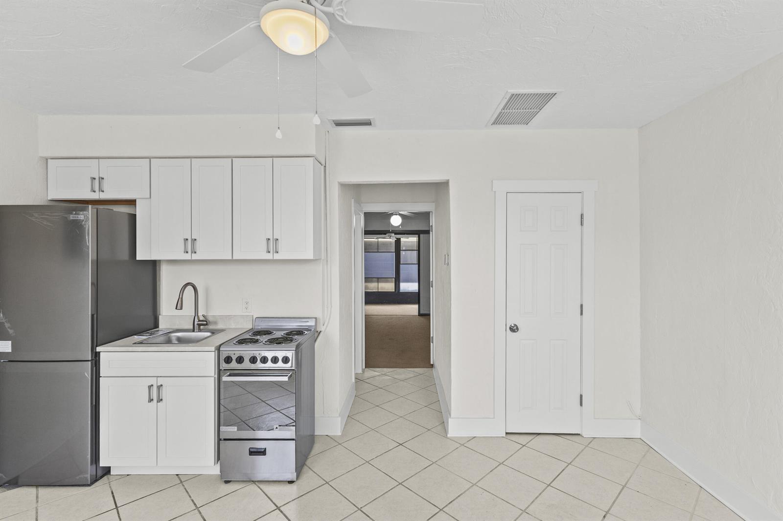 A small kitchen features white cabinets, stainless steel appliances, and light-colored tile flooring — 908 Villas Drive # 18, Venice FL 34285, VENICE, FL