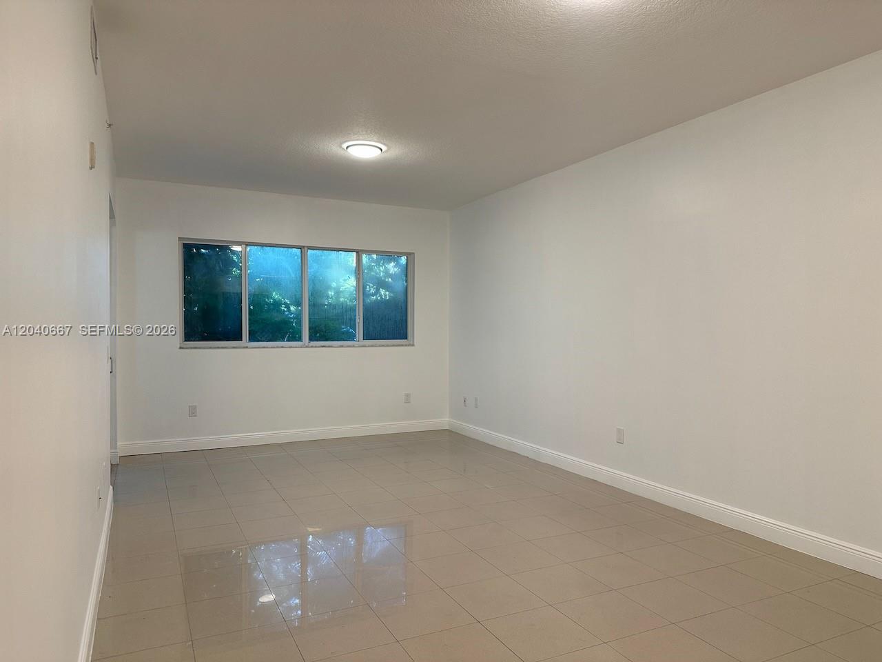 An empty room features white walls, light-colored tile flooring, and a large window — 652 NE 63rd St # 102, Miami FL 33138, MIAMI, FL