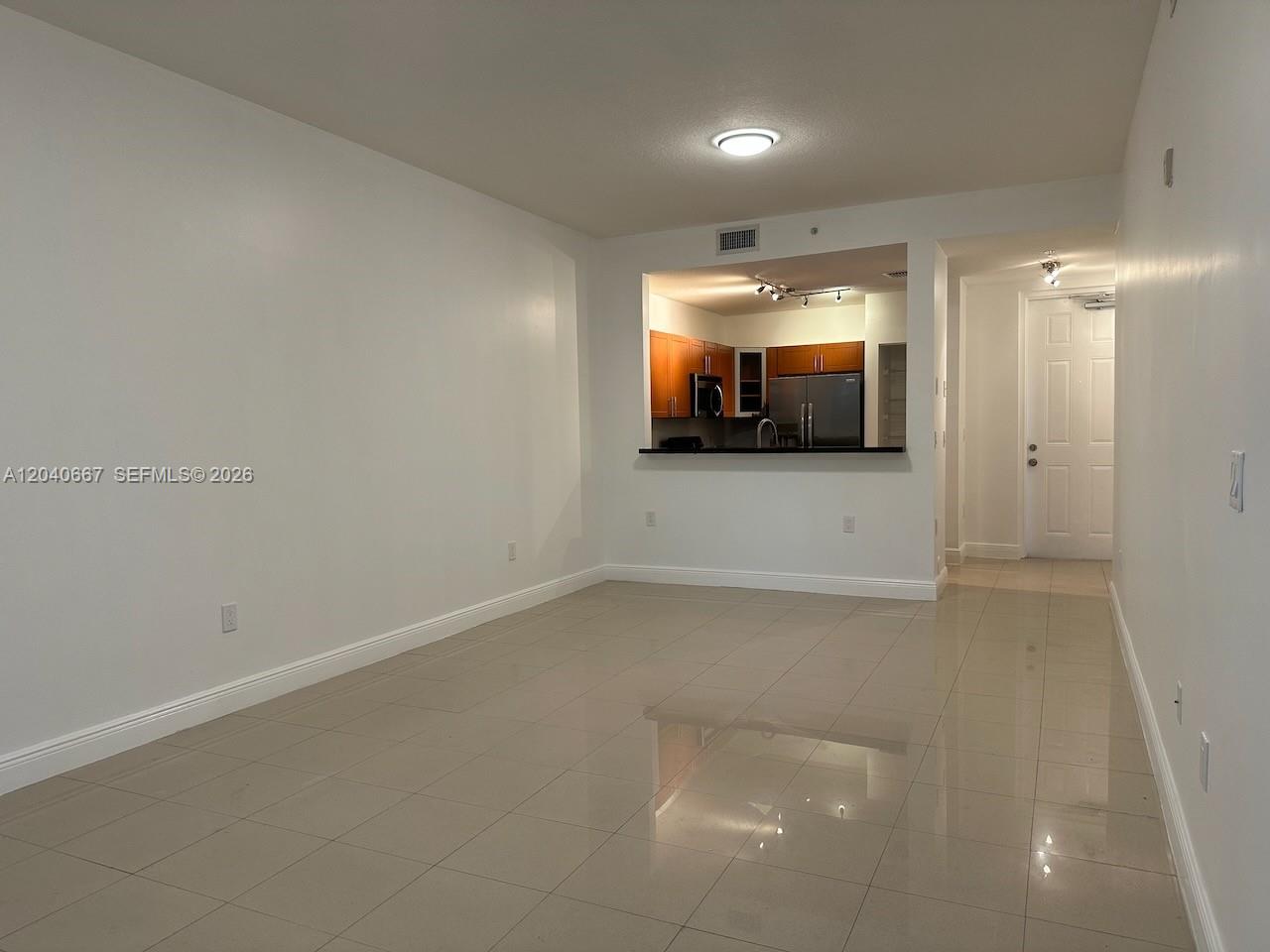 An empty room with light-colored tile flooring features a pass-through opening to a kitchen — 652 NE 63rd St # 102, Miami FL 33138, MIAMI, FL