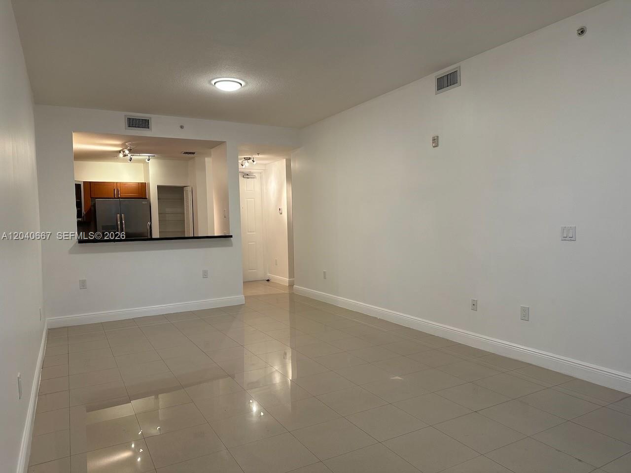 An empty living room with light-colored tile flooring features a pass-through window to the kitchen — 652 NE 63rd St # 102, Miami FL 33138, MIAMI, FL