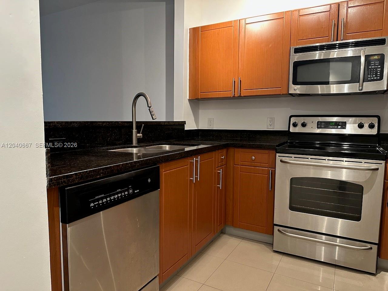 A kitchen features wood cabinets, stainless steel appliances, and dark granite countertops — 652 NE 63rd St # 102, Miami FL 33138, MIAMI, FL