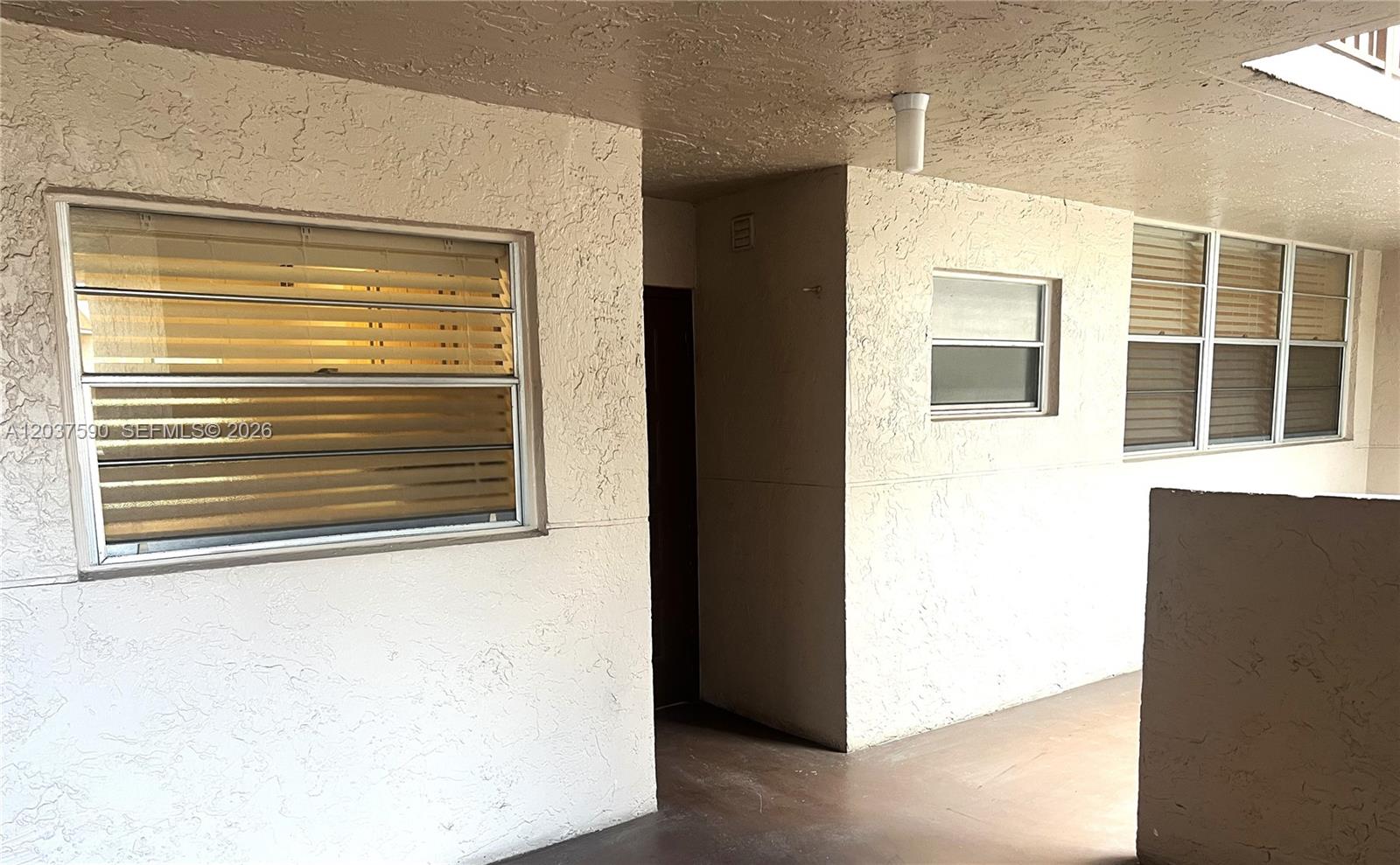 An exterior view of a building corridor with stucco walls and jalousie windows — 9531 Seagrape Dr # 305, Davie FL 33324, DAVIE, FL