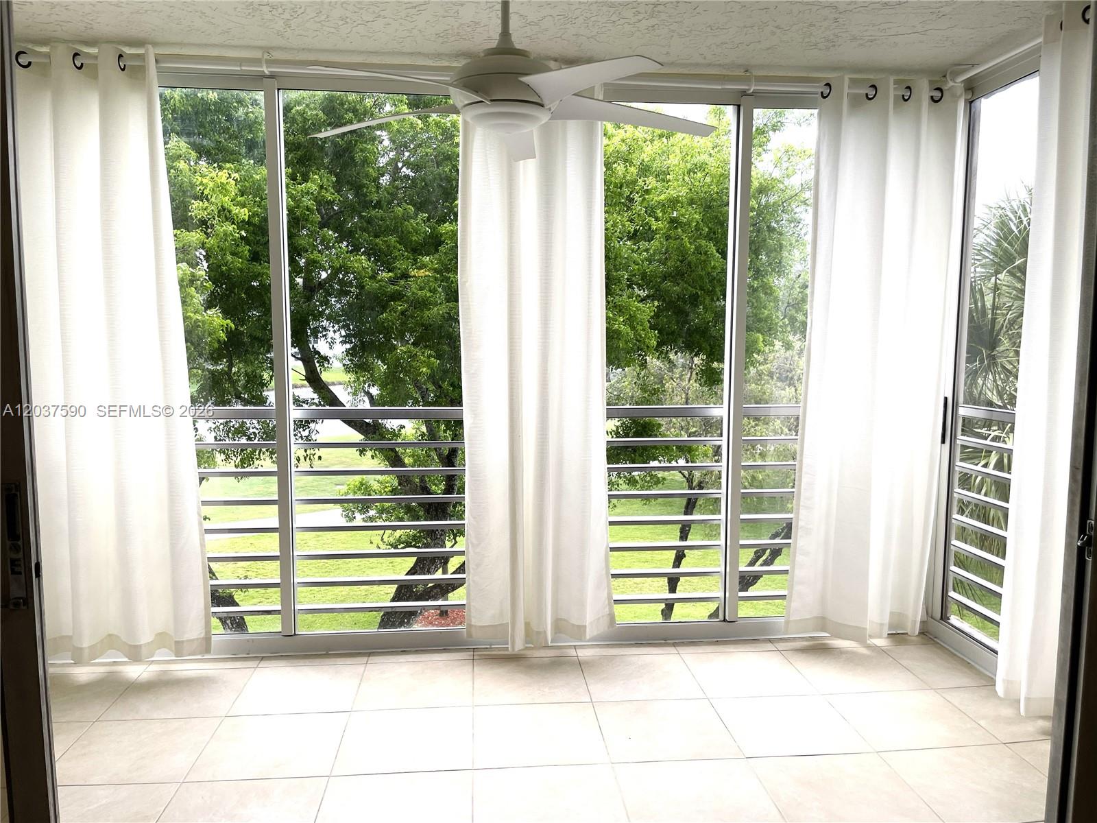 A sunroom with tile flooring, white curtains, a ceiling fan, and views of trees outside — 9531 Seagrape Dr # 305, Davie FL 33324, DAVIE, FL