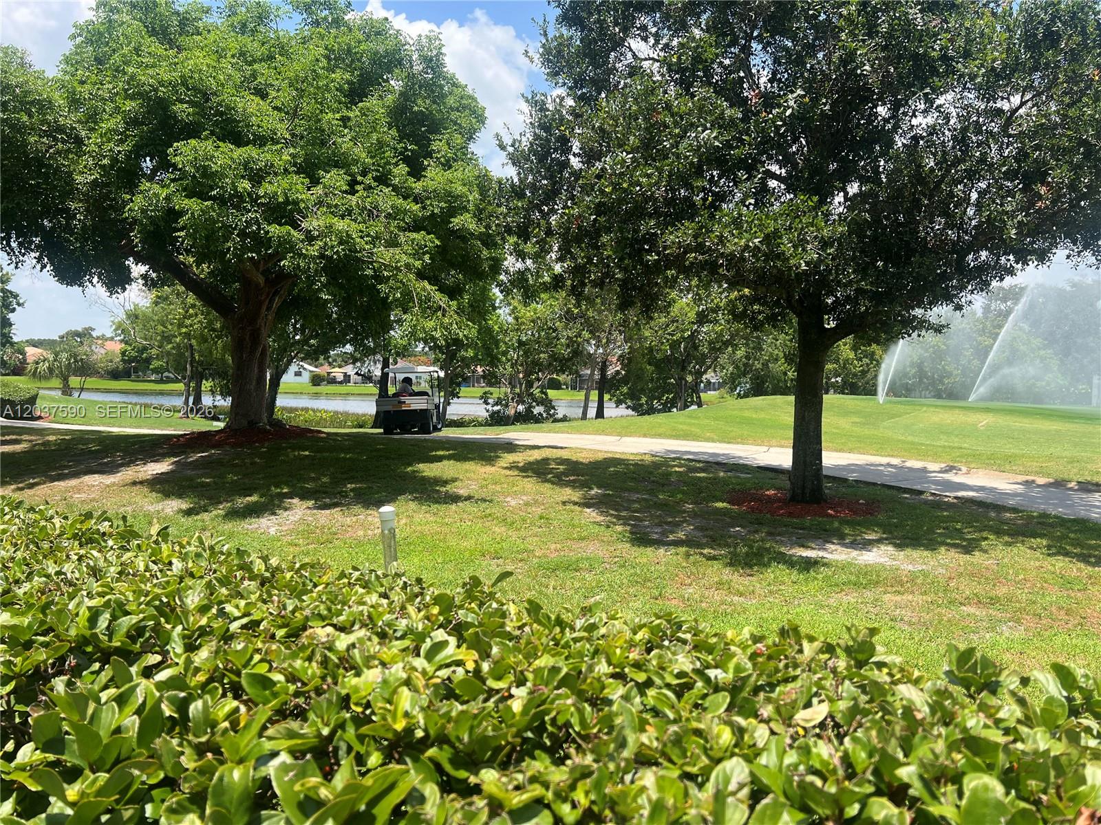 A golf cart drives along a path on a golf course with trees and sprinklers — 9531 Seagrape Dr # 305, Davie FL 33324, DAVIE, FL