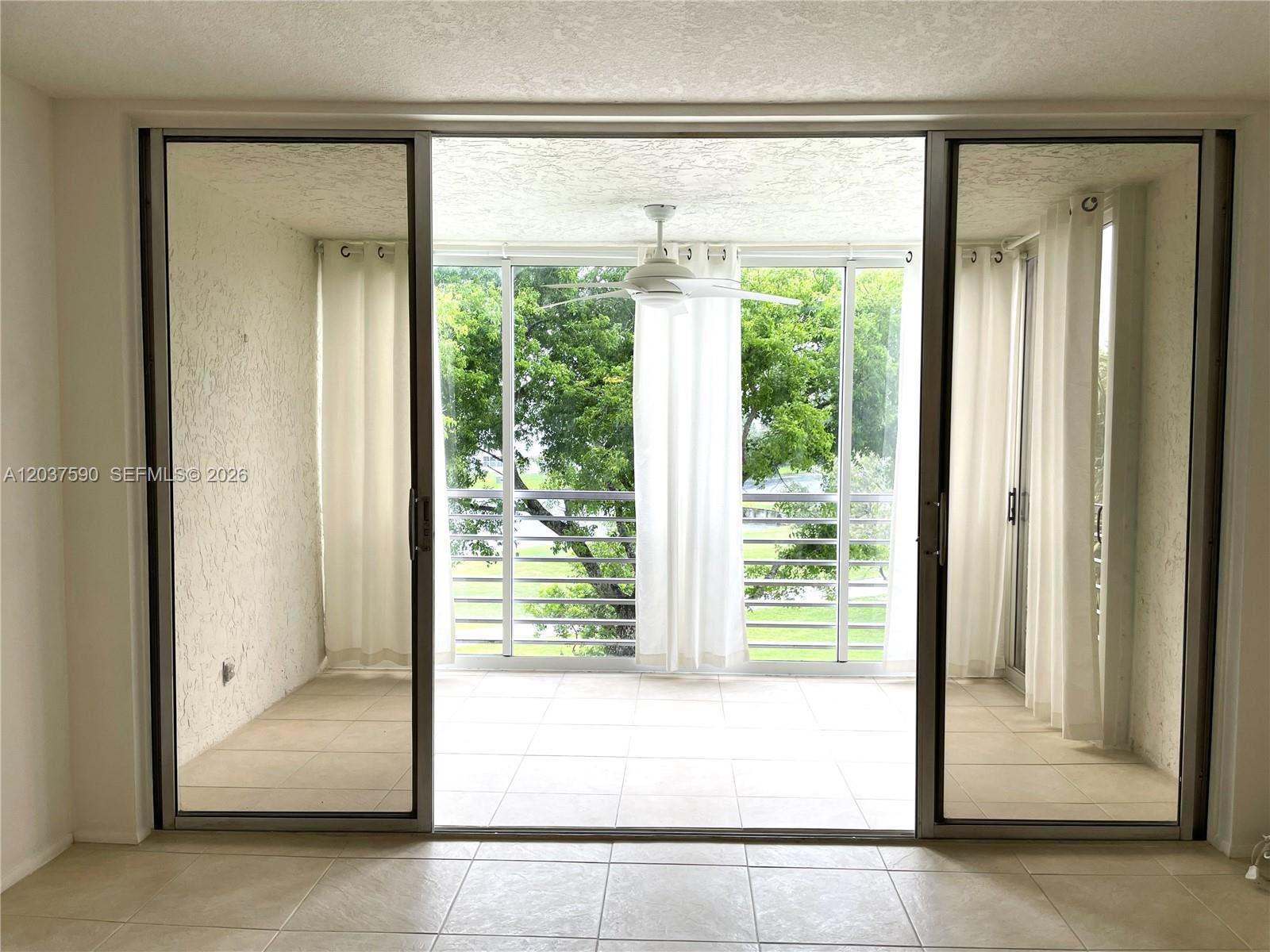 A tiled balcony with a ceiling fan and white curtains overlooks a green outdoor area — 9531 Seagrape Dr # 305, Davie FL 33324, DAVIE, FL