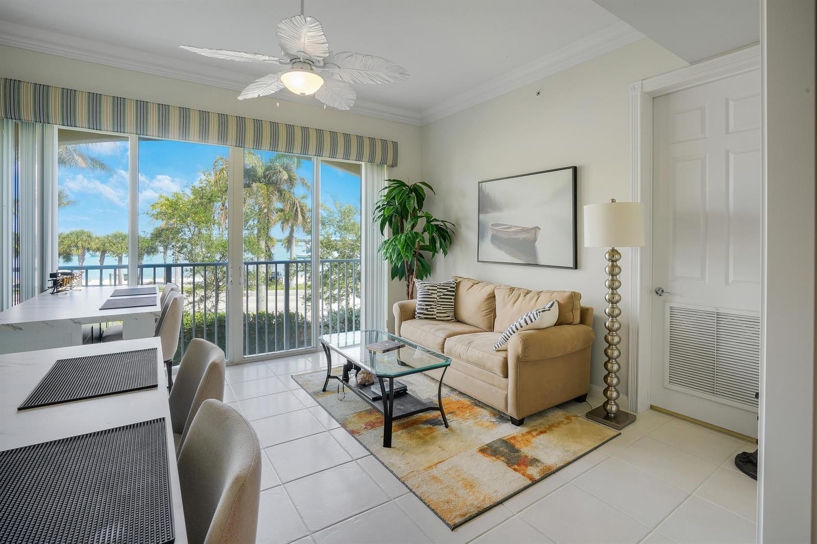 A living room with a beige sofa, glass coffee table, and a view of palm trees — FORT PIERCE, FL
