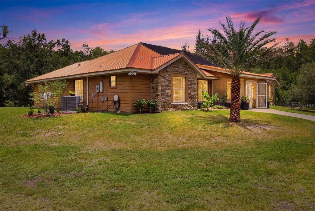 A single-story house with a metal roof, stone accents, and a palm tree in front — 12143 NE 47TH PLACE, SILVER SPRINGS, FL