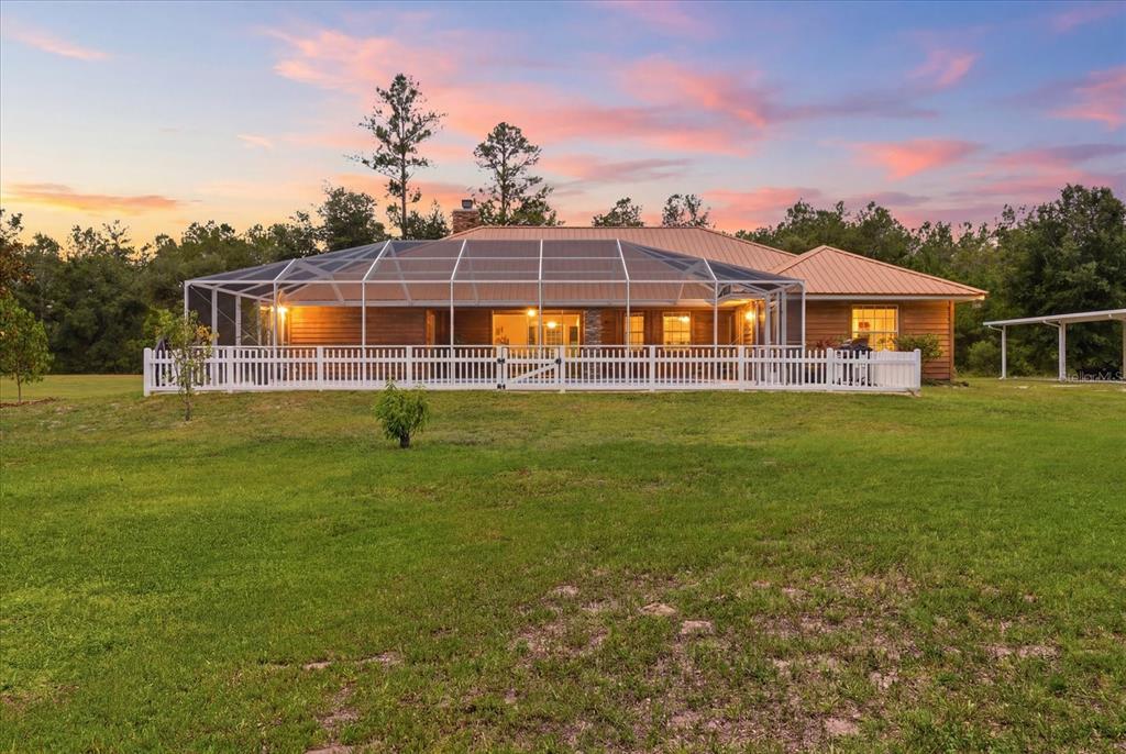 A single-story house with a metal roof and a screened-in pool enclosure at sunset — 12143 NE 47TH PLACE, SILVER SPRINGS, FL