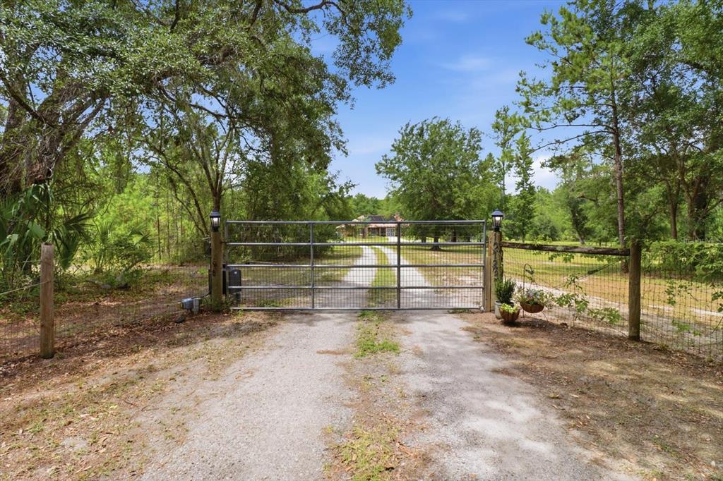 A metal gate blocks a gravel driveway leading to a house surrounded by trees — 12143 NE 47TH PLACE, SILVER SPRINGS, FL