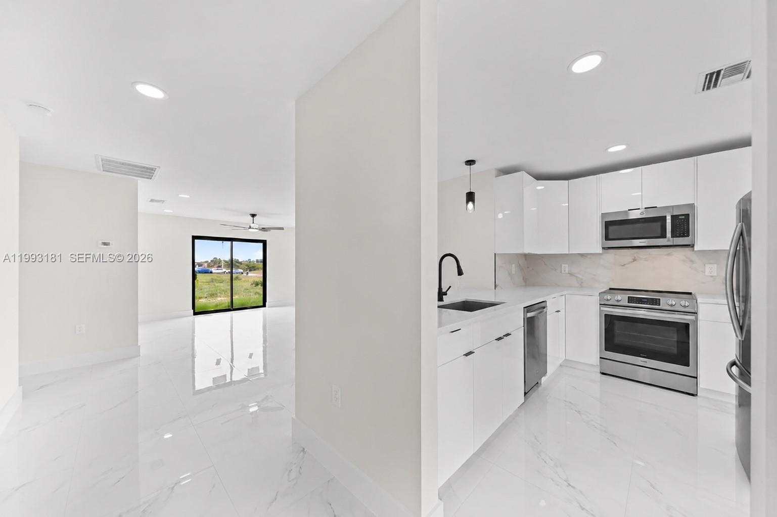 A modern kitchen with white cabinets and marble-style flooring opens into a bright living area — 2501 E 15TH ST, Lehigh Acres FL 33972, LEHIGH ACRES, FL